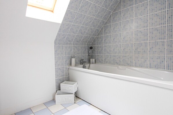 A modern bathroom with a freestanding bathtub, tiled walls, and a skylight.