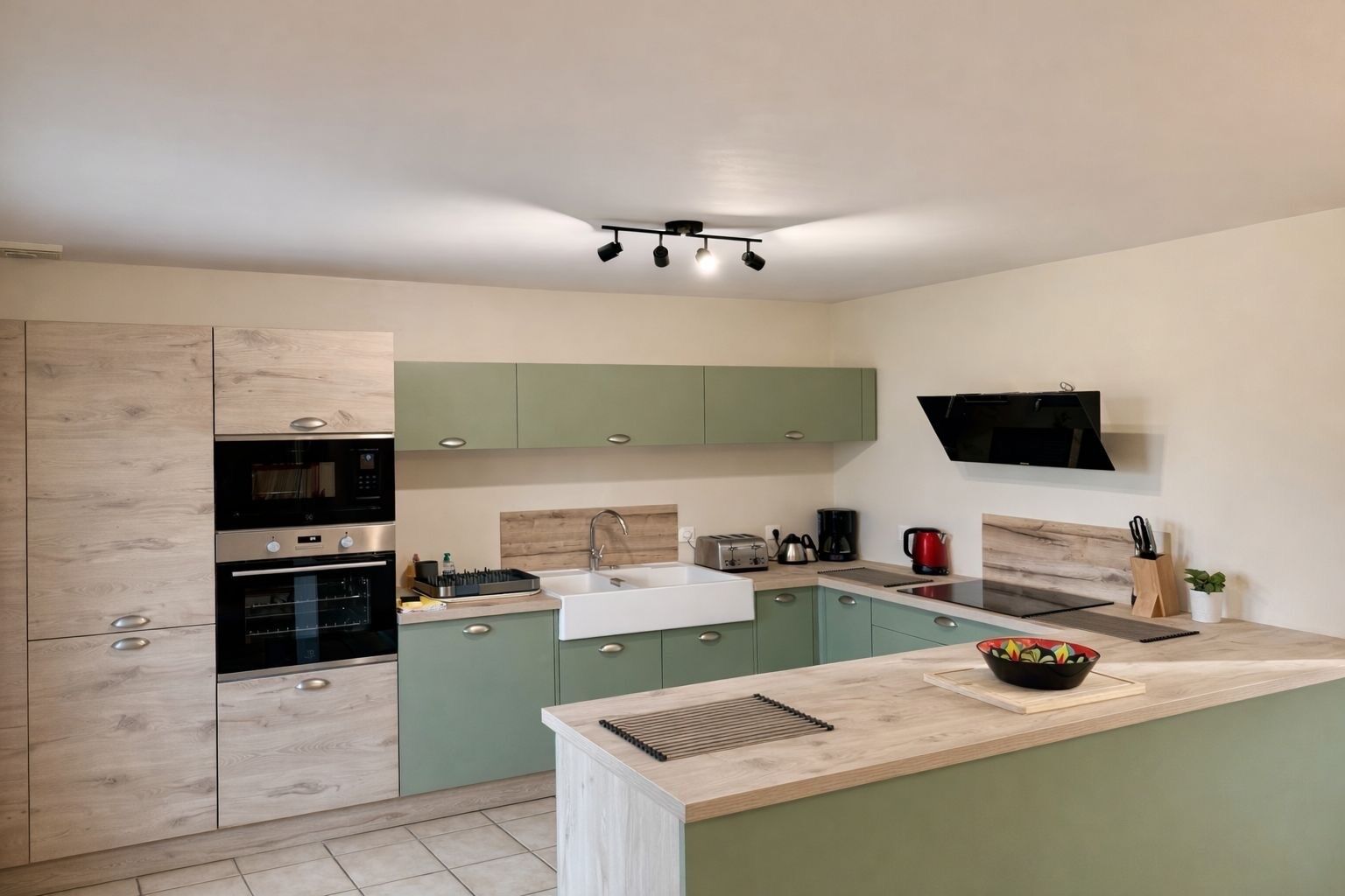 Een moderne keuken met groene kastjes, een ingebouwde oven, een spoelbak en een flatscreen televisie aan de muur.