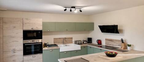 Een moderne keuken met groene kastjes, een ingebouwde oven, een spoelbak en een flatscreen televisie aan de muur.