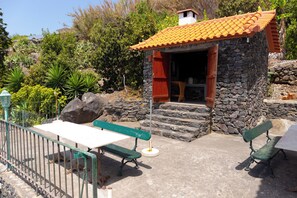 A stone building with a tiled roof, a wooden door, and a small porch area with a bench. - Luxury villa by the sea with private pool, terrace and sea view (Calheta)