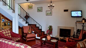 A living room with a fireplace, a television, and a staircase. - Luxury villa by the sea with private pool, terrace and sea view (Calheta)