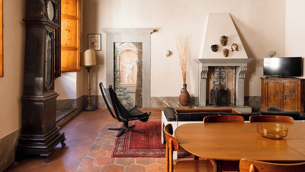 Un comedor con una mesa de madera, sillas, un reloj, una chimenea y un televisor.