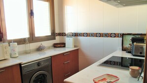 A compact kitchen with a washing machine, a toaster, and a window with blinds. - PENTHOUSE, TERRACE ON THE HORIZON OF ALMERIA (Almería)