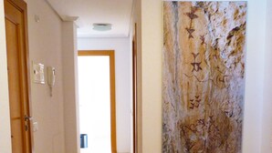 A hallway with a wooden floor, a red and black rug, a marble wall art, and a door with a phone on the wall. - PENTHOUSE, TERRACE ON THE HORIZON OF ALMERIA (Almería)