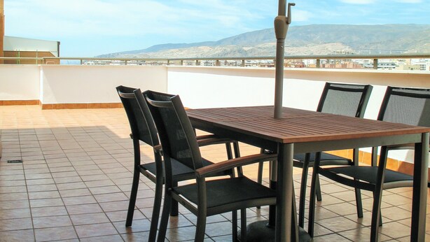 A terrace with a table and chairs, an umbrella, and a view of distant hills and a bridge. - PENTHOUSE, TERRACE ON THE HORIZON OF ALMERIA (Almería)