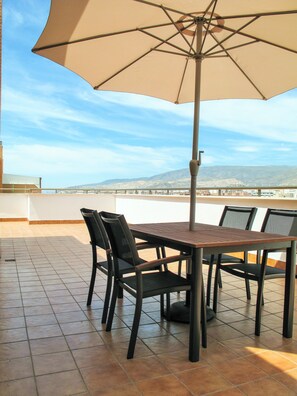 A terrace with a table and chairs, an umbrella, and a view of distant hills and a bridge. - PENTHOUSE, TERRACE ON THE HORIZON OF ALMERIA (Almería)