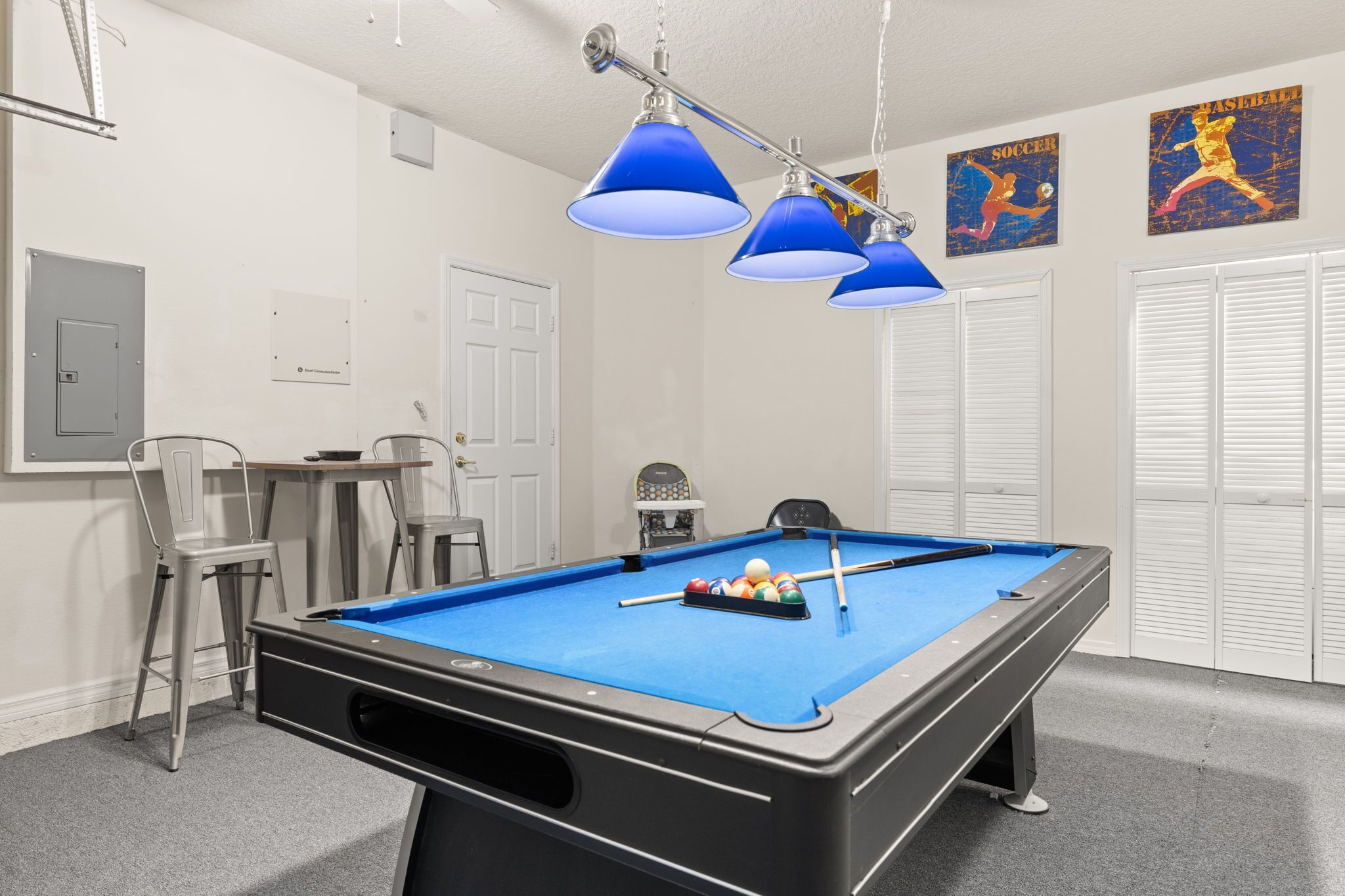 A pool table with blue felt, overhead blue lamps, and sports-themed wall art.