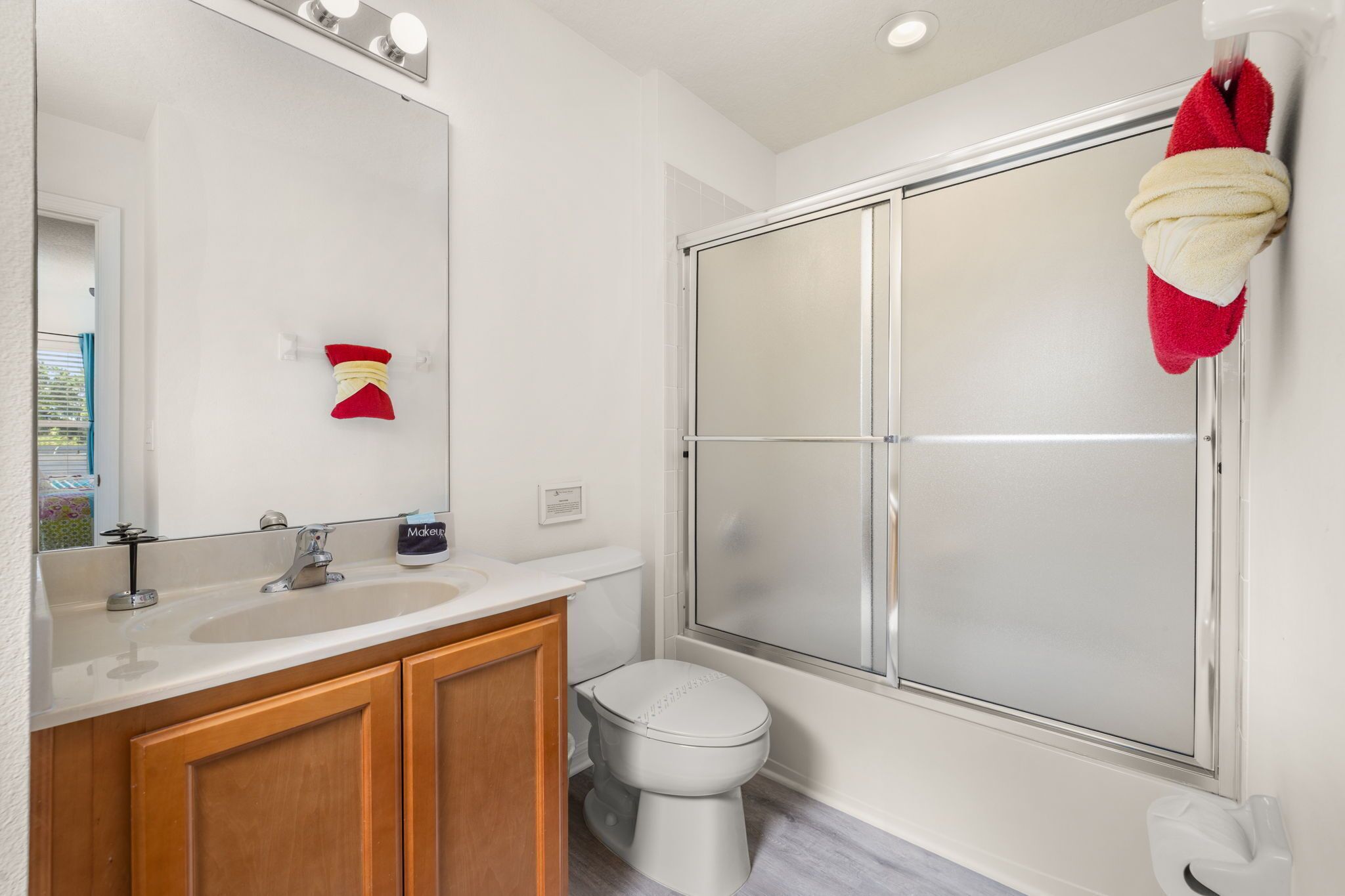 Een moderne badkamer met een wit wastafelmeubel, houten kastjes, een toilet en een douchecabine met glazen wanden.