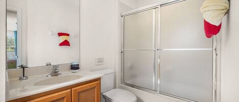 A modern bathroom with a white sink, wooden cabinets, a toilet, and a glass shower enclosure.
