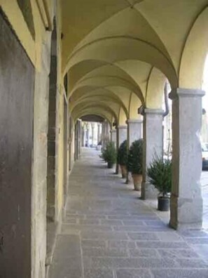 A corridor with a series of arches, stone flooring, and potted plants.