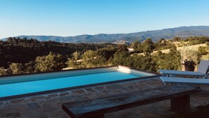 Une piscine avec un revêtement de sol en pierre, des chaises longues et une vue sur un paysage vallonné.