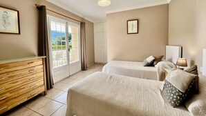 A bedroom with two beds, a wooden dresser, a ceiling light, and a view of the outdoors through a sliding door. - A spacious 4 bedroom villa, all with en suite bathrooms, large garden & Pool (calonge)