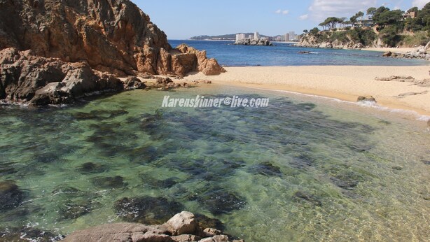 A coastal beach with clear waters, rocky outcrops, and a distant view of buildings. - A spacious 4 bedroom villa, all with en suite bathrooms, large garden & Pool (calonge)