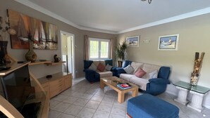 A living room with a sofa set, a coffee table, and a TV. There is a window with curtains, a plant, and artwork on the walls. - A spacious 4 bedroom villa, all with en suite bathrooms, large garden & Pool (calonge)