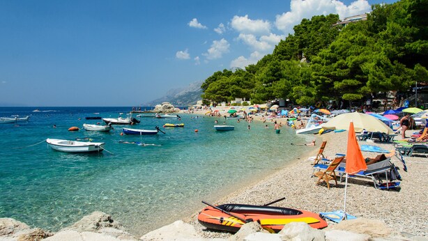 A beach with clear turquoise water, boats, and umbrellas. - Luxury Apartment in the heart of Diocletian’s Palace with large private terrace. (Split)