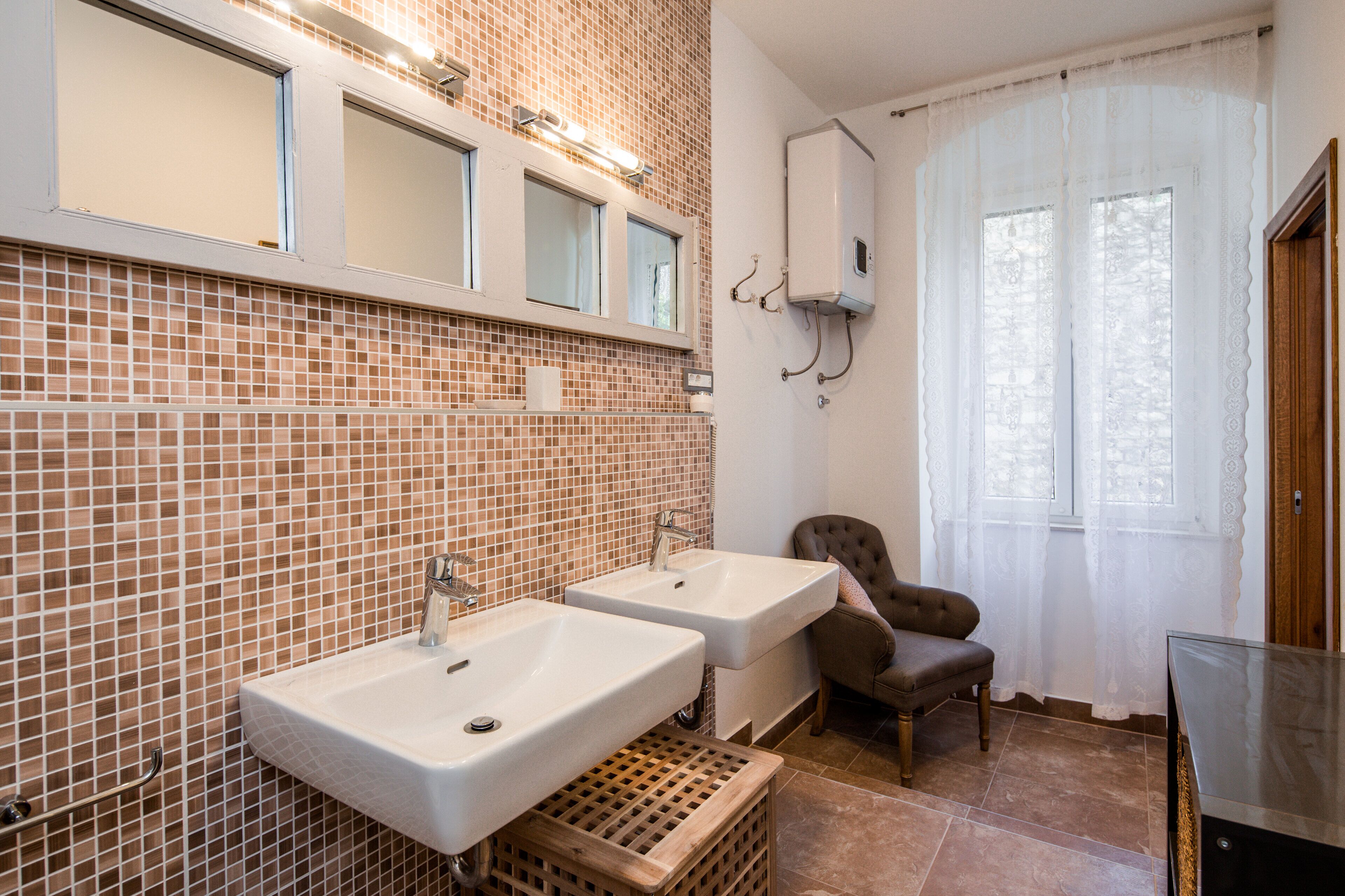 Un bagno con due lavandini, uno specchio, una finestra con tende e una cassa di legno.