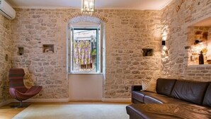 A room with stone walls, a leather sofa, a chair, and a window with curtains. - Luxury Apartment in the heart of Diocletian’s Palace with large private terrace. (Split)