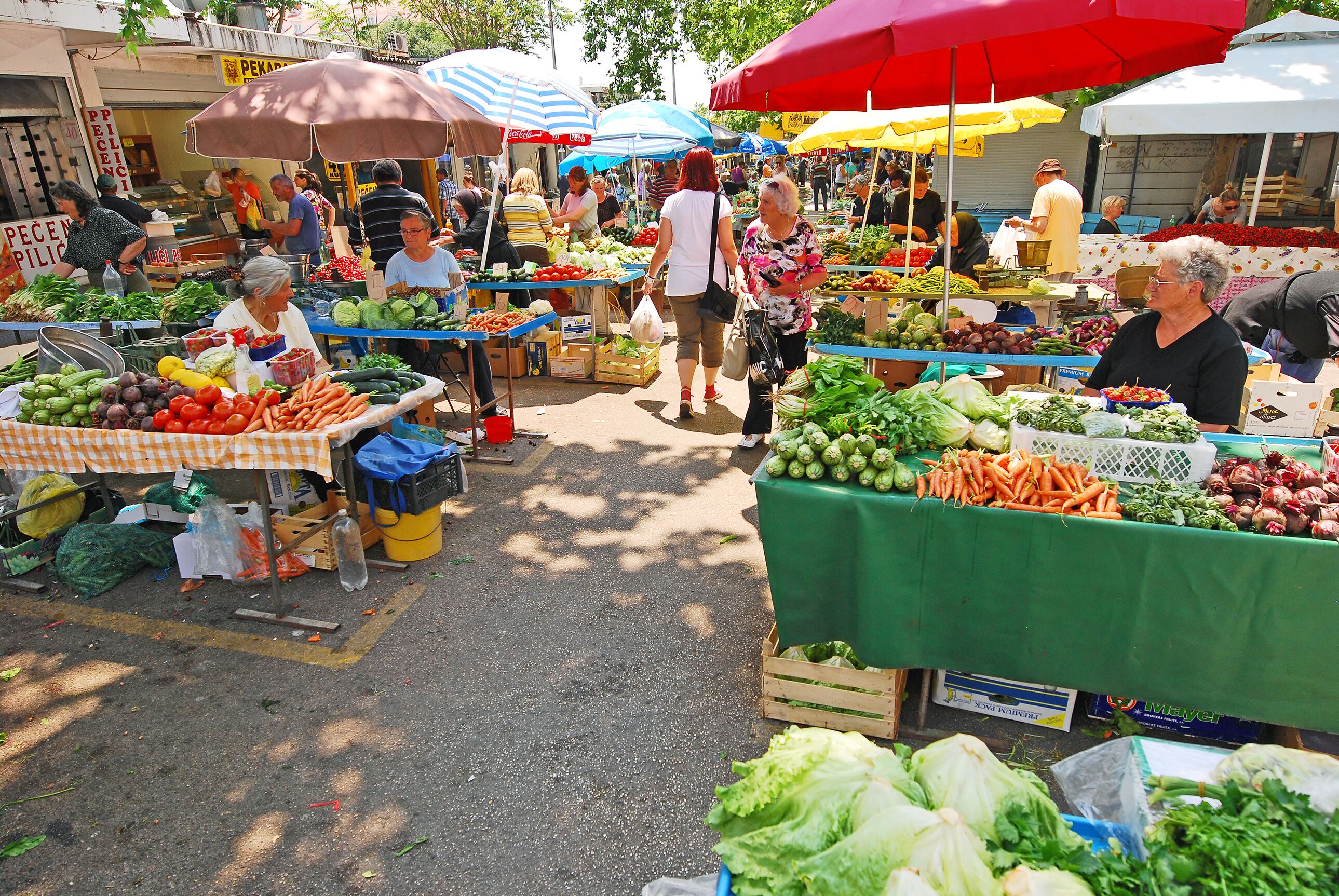 Ein Markt im Freien mit verschiedenen Ständen, auf denen frische Lebensmittel unter bunten Sonnenschirmen verkauft werden.