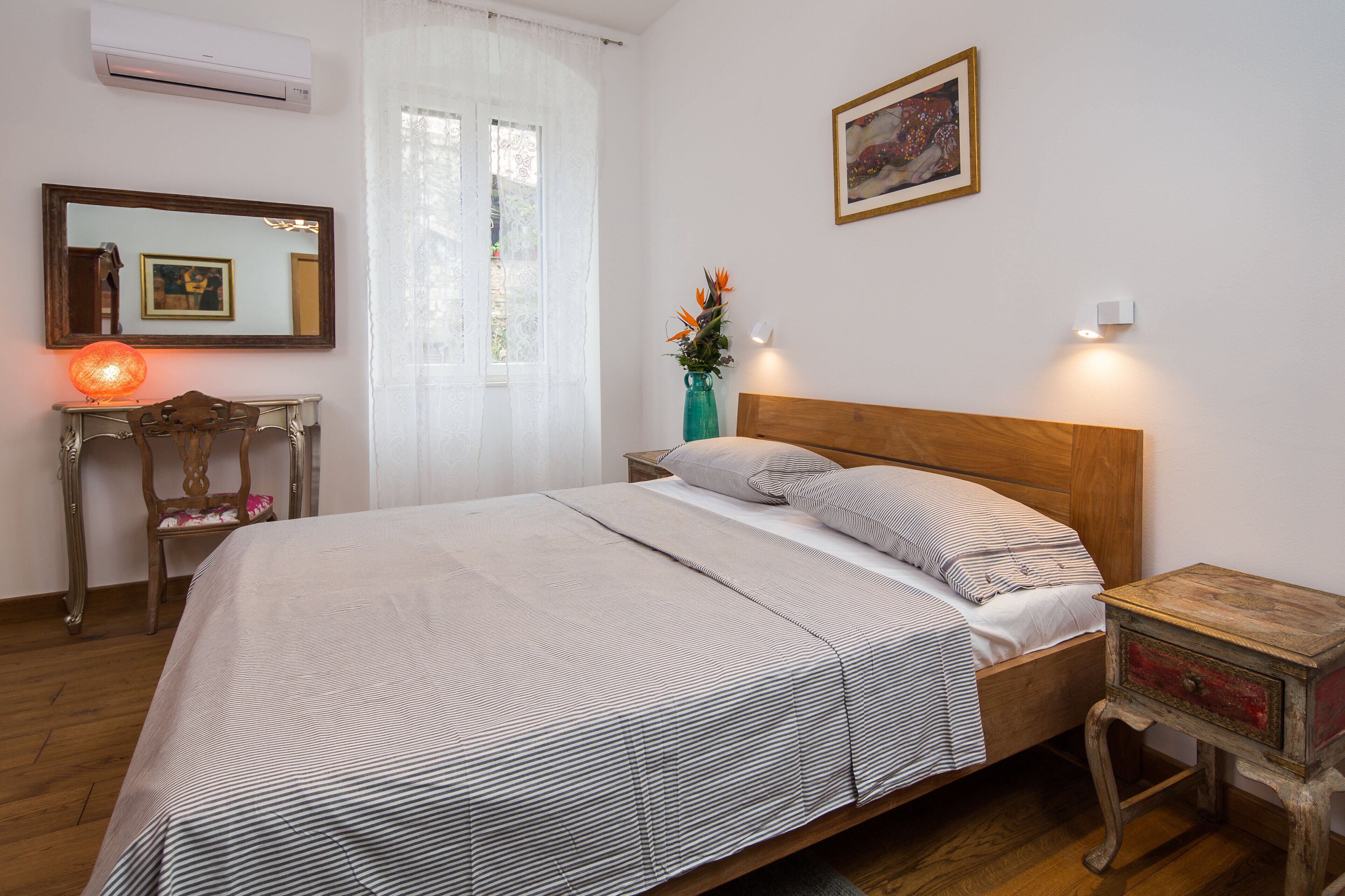 A neatly arranged bedroom with a bed, bedside table, lamp, and a mirror.