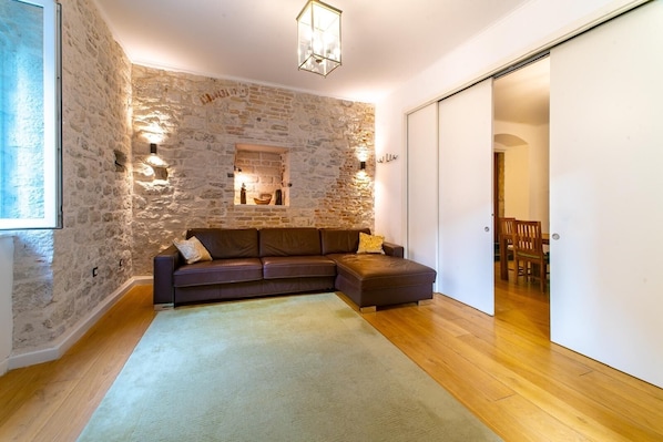 Una sala de estar acogedora con una pared de piedra, un sofá de cuero marrón, piso de madera y una puerta corredera que da a otra habitación.