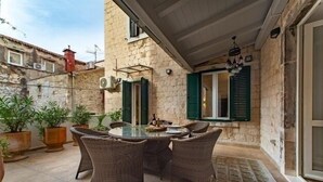 An outdoor patio with wicker furniture, potted plants, and a stone wall. - Luxury Apartment in the heart of Diocletian’s Palace with large private terrace. (Split)