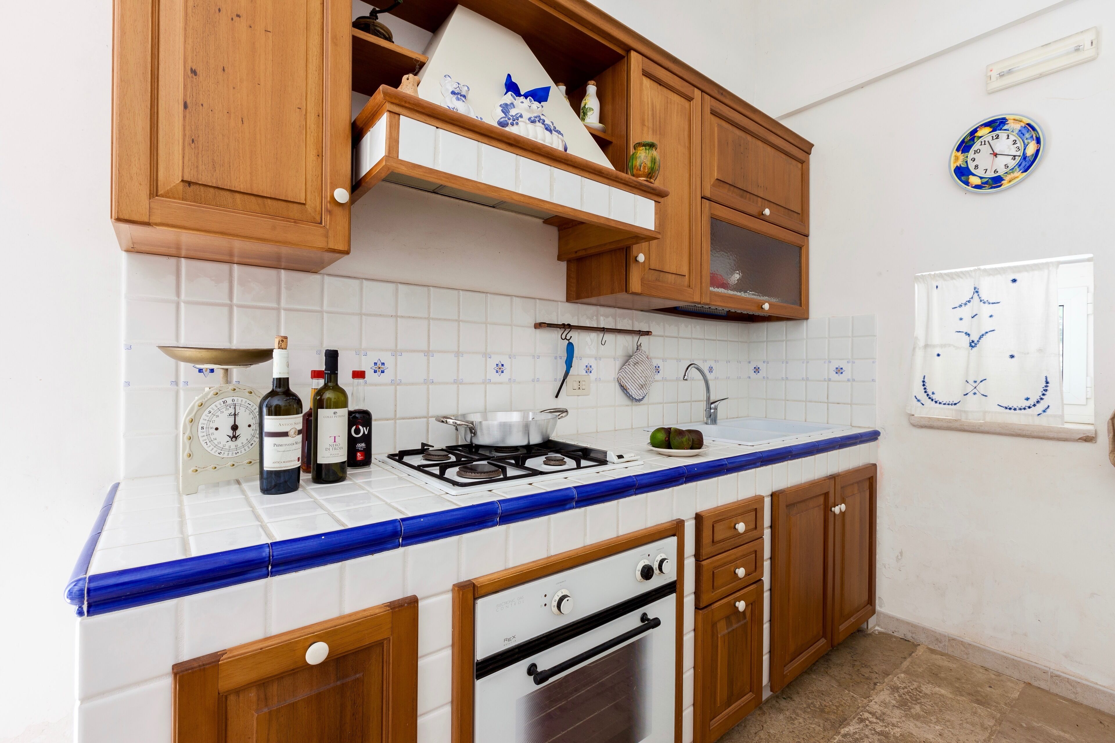 A kitchen with wooden cabinets, a gas stove, a sink, and a clock on the wall.