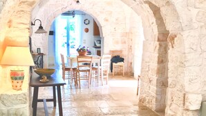 An arched stone corridor leading to a dining area with a table, chairs, and a lamp. - At Trullo Sovrano - Rental Home - Air condition and free Wi-Fi (Locorotondo)