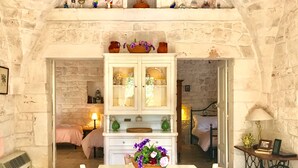 A cozy room with a stone wall, a white cabinet with glass doors, a dining table with chairs, and a bed with a pink blanket. - At Trullo Sovrano - Rental Home - Air condition and free Wi-Fi (Locorotondo)