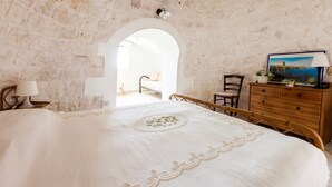 A bedroom with a stone wall, a wooden bed, a dresser, and a lamp. - At Trullo Sovrano - Rental Home - Air condition and free Wi-Fi (Locorotondo)