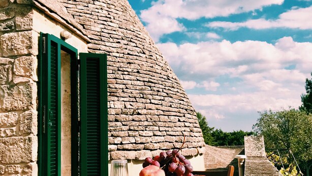 A stone building with a conical roof, a table with breakfast items, and a clear blue sky. - At Trullo Sovrano - Rental Home - Air condition and free Wi-Fi (Locorotondo)