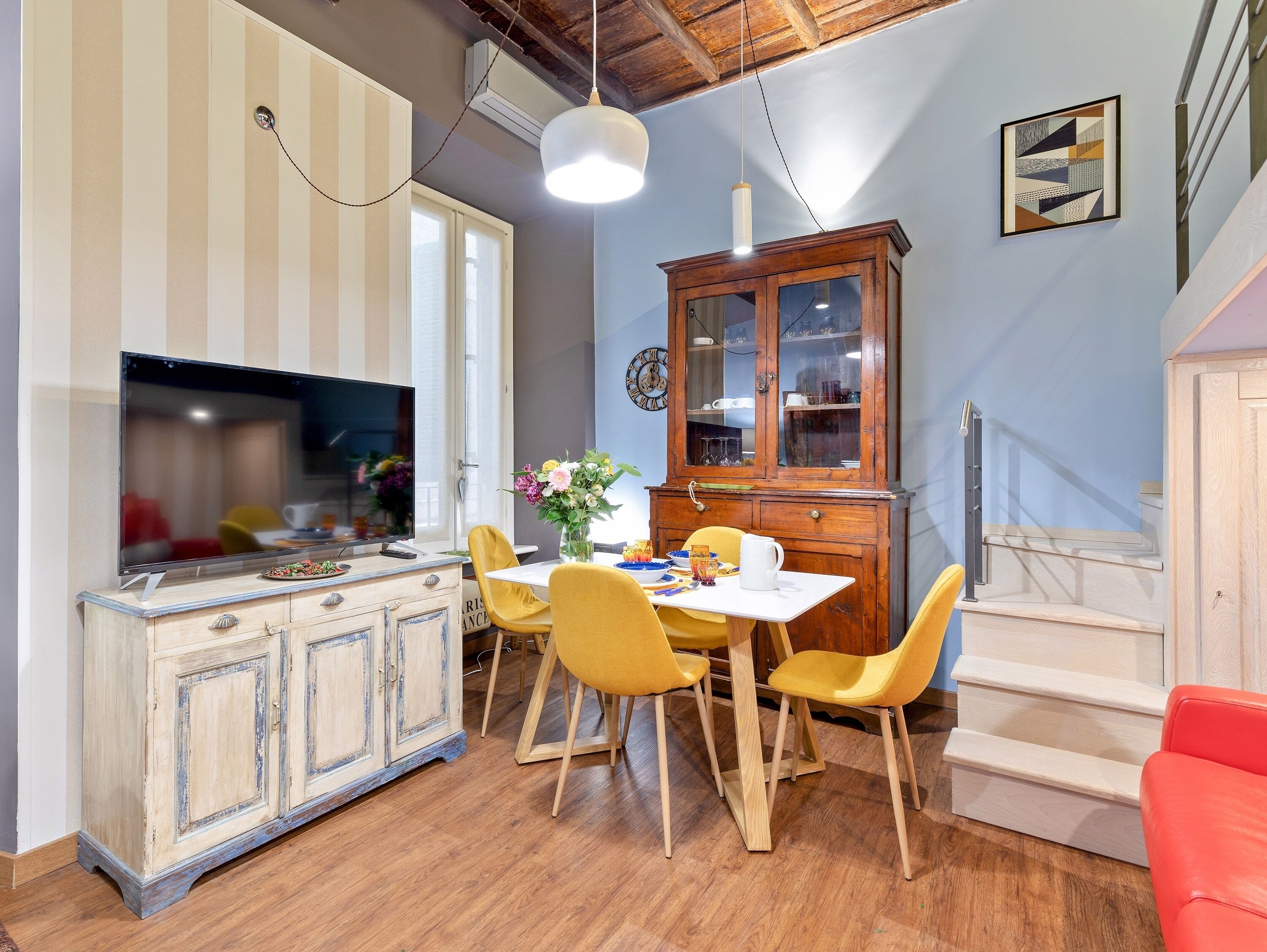 A dining area with a wooden cabinet, yellow chairs, and a white table.