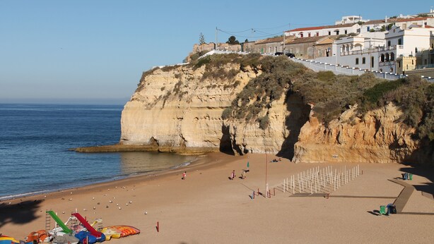 Una playa costera con un acantilado, sombrillas y un parque infantil.