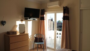 Un dormitorio con cama, cómoda, silla, televisor y puerta corrediza a un balcón.