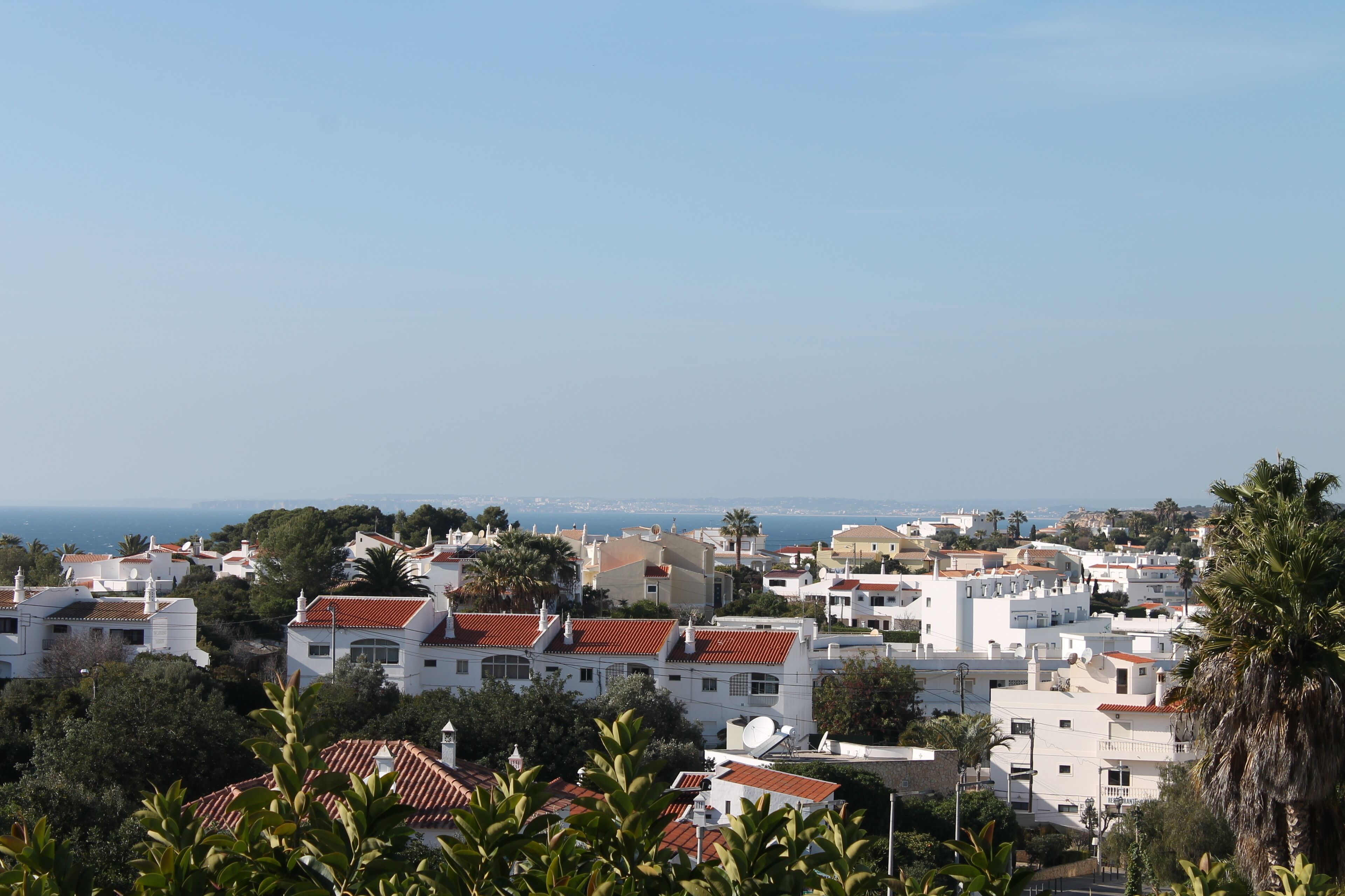 Une ville côtière aux bâtiments blancs et aux toits recouverts de tuiles rouges, entourée de verdure et offrant une vue sur la mer.