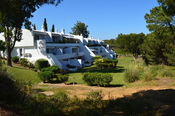 A modern white building with multiple balconies, surrounded by well-maintained lawns and trees. - T1 Duplex in Victory Village - Quinta do Lago (Almancil - ALGARVE)