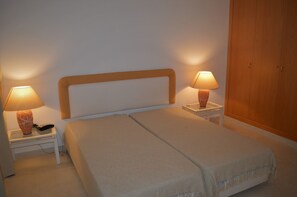 A double bed with a wooden headboard, two bedside tables with lamps, and a wooden wardrobe. - T1 Duplex in Victory Village - Quinta do Lago (Almancil - ALGARVE)