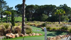 A golf course with a putting green, surrounded by various types of vegetation and rocks. - T1 Duplex in Victory Village - Quinta do Lago (Almancil - ALGARVE)