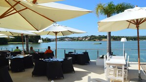 An outdoor dining area with tables and chairs, umbrellas, and a view of a lake. - T1 Duplex in Victory Village - Quinta do Lago (Almancil - ALGARVE)