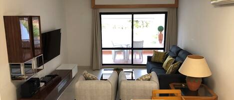A modern living room with a sofa, two armchairs, a coffee table, a TV, and a lamp.