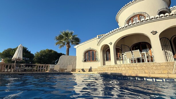A poolside area with a palm tree, outdoor furniture, and a building with arches and a round tower.