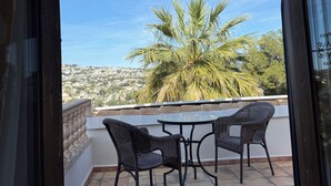 A balcony with a table and chairs, a view of a palm tree, and a distant town.