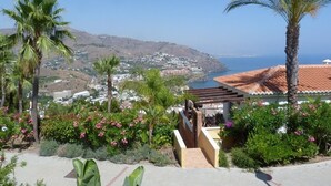 A coastal view with a building featuring a red-tiled roof, surrounded by lush greenery and palm trees. - HOLIDAYS WITH SEA AND MOUNTAIN VIEWS (ALMUÑECAR - GRANADA)