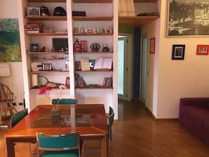 Ein Wohnzimmer mit einem Holzesstisch, Stühlen, einem Bücherregal und einem violetten Sofa.