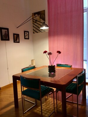 Ein Essbereich mit einem Holztisch, grünen Polsterstühlen, einer Blumenvase und gerahmten Bildern an der Wand.