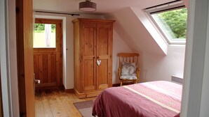 A bedroom with a wooden wardrobe, a bed with a pink bedspread, a chair, and a skylight. - Traditional Breton Longere, Cotes d'Armor (La Chapelle-Neuve)