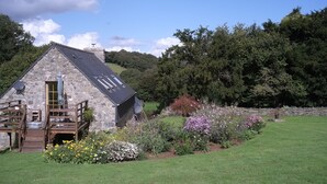A stone house with a wooden deck and a garden with various flowers. - Traditional Breton Longere, Cotes d'Armor (La Chapelle-Neuve)