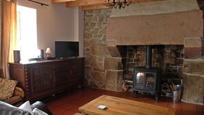 A cozy living room with a stone fireplace, a wooden coffee table, a leather sofa, and a television on a wooden cabinet. - Traditional Breton Longere, Cotes d'Armor (La Chapelle-Neuve)
