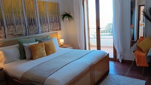 Une chambre d’hôtel avec un grand lit, une table de chevet avec une lampe, une vue sur l’extérieur grâce à une porte-fenêtre coulissante et un tableau au mur.