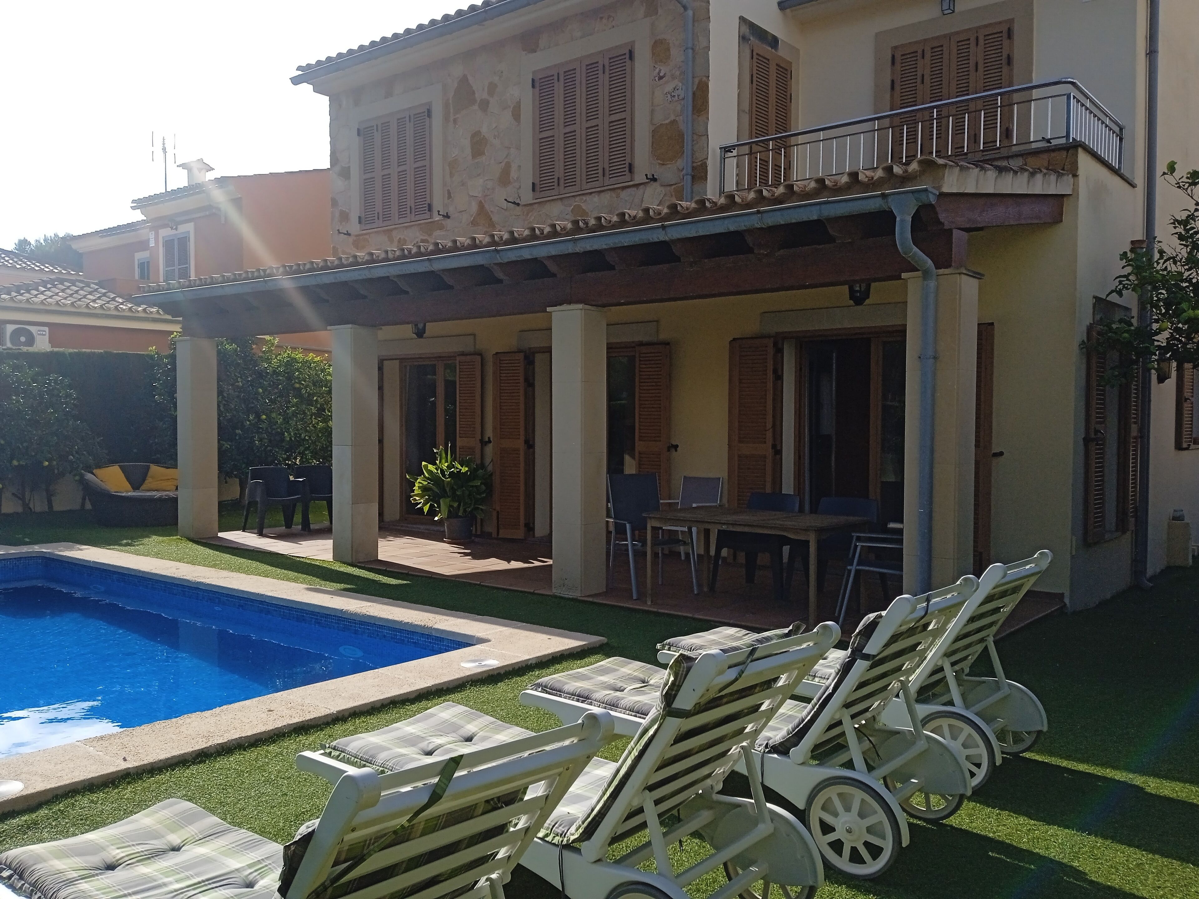 Una casa de dos pisos con piscina, mobiliario exterior y un patio cubierto.
