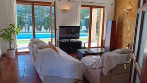 Une pièce avec un long canapé, un téléviseur et une petite table. On y trouve une plante en pot et une statue accrochée au mur.